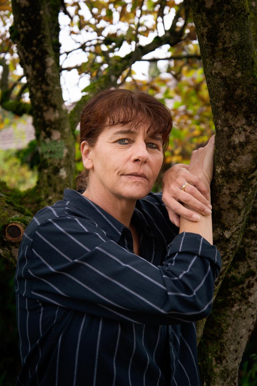 Catherine Lovey, femme brune aux cheveux longs, la cinquantaine, pose l'air serein et heureux, de trois quart face à l'objectif sur son profil droit.